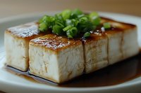 Grilled tofu blocks with soy sauce and fresh green onions on white plate. Healthy vegetarian protein dish for Asian cuisine and plant-based cooking.