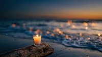 Glowing candle on driftwood at ocean shore during sunset with bokeh lights reflecting on waves creating peaceful meditation atmosphere for relaxation.