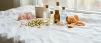 Natural spa wellness setup with essential oil bottles, himalayan salt crystals and citrus fruits on white bedding for aromatherapy relaxation treatments.