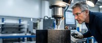 Senior male engineer inspecting carbon fiber component on precision CNC machine in modern manufacturing facility for quality control and production.