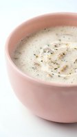 Creamy mushroom soup with herbs and spices served in pink ceramic bowl on white background for culinary and restaurant menu design.