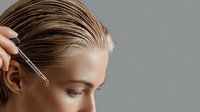 Young Caucasian woman receiving hair oil treatment with dropper, side view profile showing wet slicked back blonde hair and natural makeup, wellness and haircare concept.
