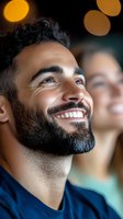 Happy young Middle Eastern man with beard smiling and looking up with warm bokeh lights in background during evening celebration or event.