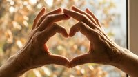 Hands forming heart shape against warm sunlit window with bokeh lights creating romantic atmosphere for love and affection concepts.