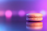 Pink macaron cookie with reflection on glossy surface against blurred purple and blue bokeh background, creating dreamy pastel atmosphere.