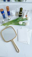 Luxury skincare products arranged on marble surface with golden mirror, white tulips and blank cards for beauty routine flatlay composition.