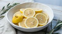 Fresh lemon slices in white ceramic bowl with olive branches on marble surface for healthy cooking and natural wellness lifestyle.