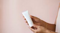 Close-up of hand holding blank white cosmetic tube against soft pink background, suitable for skincare, beauty product packaging mockups and advertising campaigns.