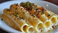 Creamy cannelloni pasta with melted cheese sauce garnished with fresh herbs and crispy breadcrumbs on white plate, close up view of traditional Italian cuisine.