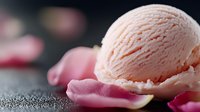 Creamy peach-colored ice cream scoop on dark surface with scattered pink rose petals creating romantic mood, soft focus background with bokeh effect.