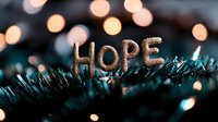 Glittering gold HOPE text on dark evergreen branches with soft bokeh lights creating magical holiday atmosphere, inspiring message of faith and optimism.