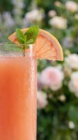 Chilled grapefruit cocktail in a tall glass garnished with fresh mint and citrus slice, set against a soft floral garden background.