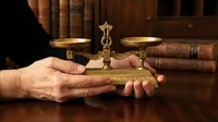 Hands holding vintage brass balance scales in library setting with old books, symbolizing justice, law, and legal decision-making in professional environment.