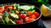 Fresh quinoa bowl with avocado, cherry tomatoes, cucumber, pine nuts and herbs served on dark background. Healthy vegan lunch with citrus dressing.