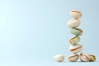 Stacked pistachio nuts balancing on light blue background, demonstrating stability and natural food composition. Creative minimal food photography.