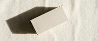 Blank white business card mockup with shadow on textured beige paper background for branding and corporate identity design projects.