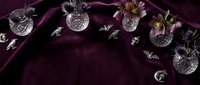 Elegant crystal glassware and pink flowers arranged on luxurious purple velvet fabric creating sophisticated table setting for special occasions and celebrations.
