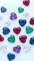 Colorful heart-shaped gemstones including sapphires, rubies, emeralds, amethysts and diamonds scattered on white background for jewelry design and luxury concepts.