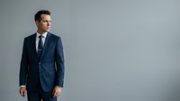 Young adult male, Caucasian, wearing navy blue business suit with tie, standing against neutral gray background, suitable for corporate, professional, and business-related projects.