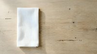 White folded napkin or kitchen towel on wooden table surface, ready for mockup, branding, or product presentation designs.