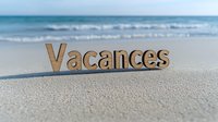 Wooden word Vacances on sandy beach with turquoise ocean waves in background, summer holiday concept for travel and leisure marketing.