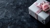 White gift box with pink satin ribbon and fresh rose on dark textured background with copy space. Romantic present concept for Valentine's day or wedding.
