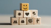 Wooden blocks with positive symbols including smiley face, heart, star, and people icons stacked in pyramid formation against soft blue background.