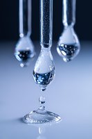 Macro shot of water drops falling from glass test tubes creating ripple effect on blue background, scientific laboratory research concept for chemistry experiments.