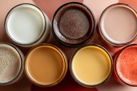 Assortment of colorful plant-based milk alternatives in glass jars viewed from above, including chocolate, vanilla, strawberry and neutral varieties.