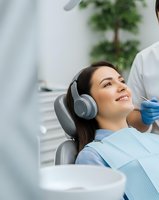 Young woman relaxing in dental chair wearing headphones during treatment at modern clinic. Patient comfort and anxiety reduction in dentistry.