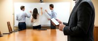 Business professional using tablet during corporate presentation meeting with colleagues at whiteboard in modern conference room.