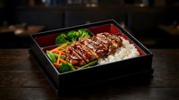 Grilled chicken teriyaki bento box with steamed rice and fresh vegetables served in traditional black lacquered container on wooden table for Asian cuisine.