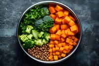 Fresh bowl with diced butternut squash, chickpeas, broccoli florets and parsley on dark background. Healthy plant based meal preparation.