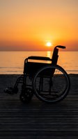 Silhouette of empty wheelchair on wooden boardwalk facing ocean at golden sunset, symbolizing hope, accessibility, and freedom for inclusive lifestyle and wellness concepts.