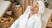 Young woman relaxing in white bathrobe and towel at luxury spa resort, enjoying wellness treatment with healthy snacks on wooden tray in serene setting.