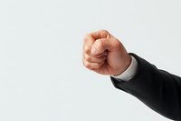 Raised fist of Caucasian businessman in black suit sleeve showing power, strength and determination against light background. Professional leadership concept.