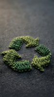 Green recycling symbol made from natural rope fibers on dark textile background representing eco-friendly sustainability and environmental awareness.