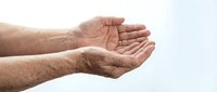 Elderly man's wrinkled hands cupped together in receiving or giving gesture on white background. Concept of care, support, charity and assistance.