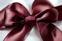 Elegant burgundy satin ribbon bow with delicate stitched edges against white background, macro photography showing luxurious fabric texture and soft shadows.