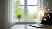 Smart home automation concept with laptop displaying digital security icons and connected device symbols on wooden desk near bright window.