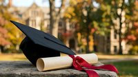 Graduation cap and diploma with red ribbon on wooden surface with blurred autumn campus background. Academic achievement and university education concept.