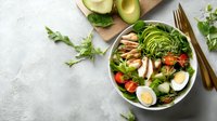 Fresh chicken and avocado salad bowl with sliced eggs, tomatoes, and greens on concrete background, healthy protein-rich meal.
