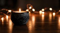 Decorative black ceramic candle holder with lit flame surrounded by warm glowing string lights creating cozy atmospheric ambiance for relaxation and meditation.