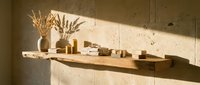 Minimalist wooden shelf with ceramic pottery and dried pampas grass against textured concrete wall in warm natural sunlight for modern interior design.