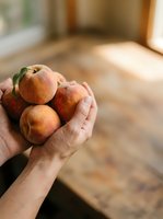 Person holding fresh ripe peaches in palm of hand indoors with natural sunlight streaming through window, showcasing organic fruit harvest and healthy eating lifestyle.