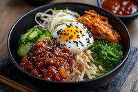 Korean bibimbap bowl with sunny side up egg, kimchi, cucumber, seaweed, rice and spicy meat topped with sesame seeds, served in black ceramic bowl.