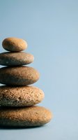 Stack of five smooth volcanic pumice stones balanced in zen tower formation on light blue background for spa wellness meditation and mindfulness concepts.