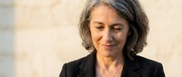 Mature woman with gray hair wearing black blazer, looking down with gentle expression, professional portrait for business and corporate use.