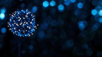 Glowing dandelion silhouette with bright blue lights against dark background creates magical atmosphere. Dreamy bokeh effect adds depth and enchantment to nature-inspired scene.