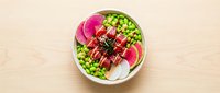 Fresh tuna poke bowl with edamame, watermelon radish, and sesame sauce served in a ceramic bowl on a light wooden surface, top view.